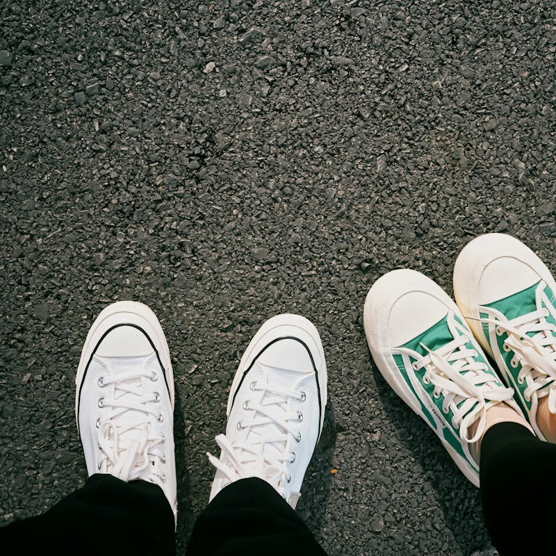 Two pairs of sneakers on asphalt ground